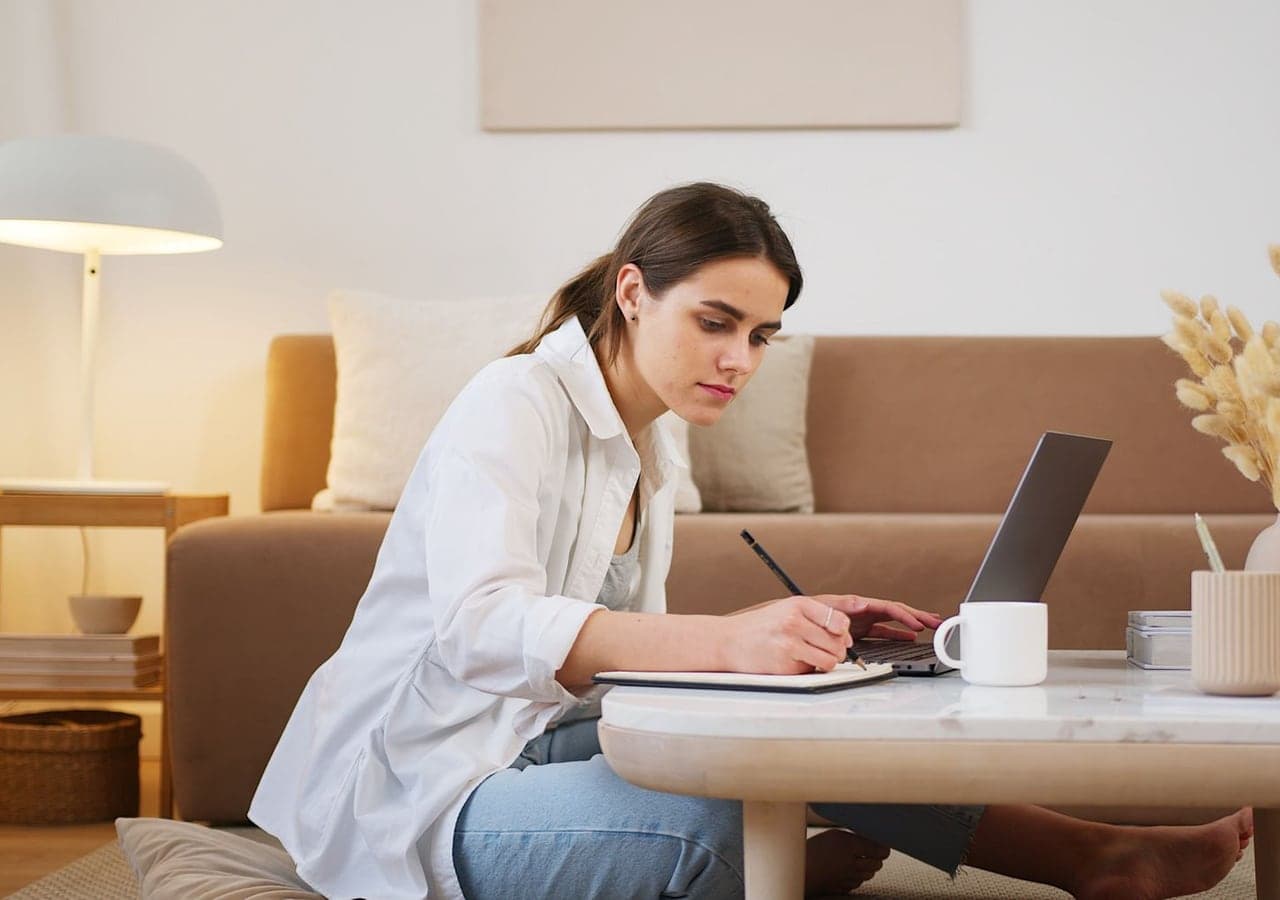 A woman taking notes beside her laptop in a bright living room