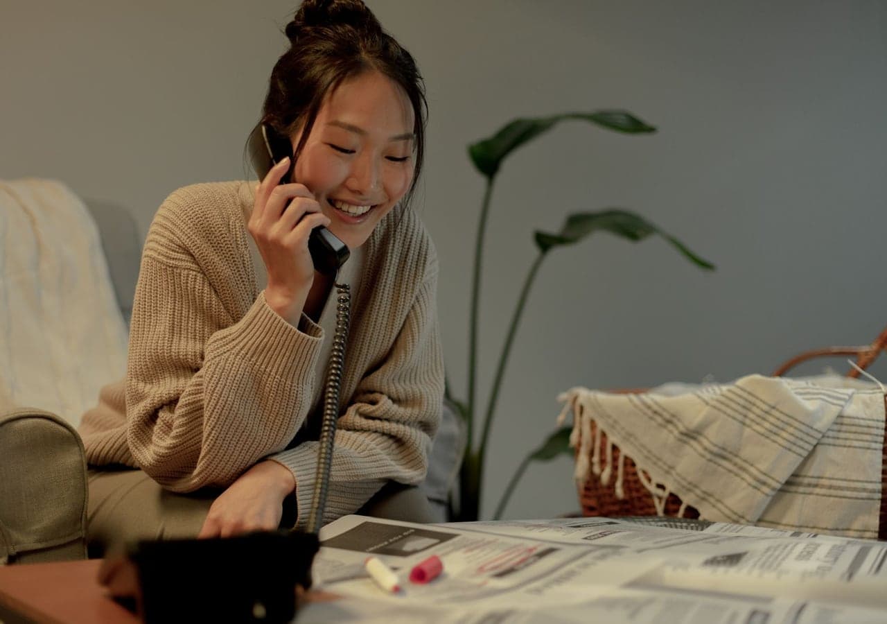 A smiling young woman talking on the phone at a table in her living room