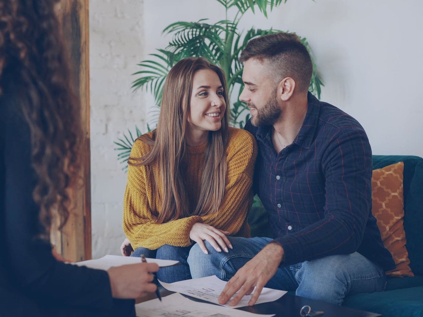 A young couple smiling on a sofa while meeting with an advisor over paperwork