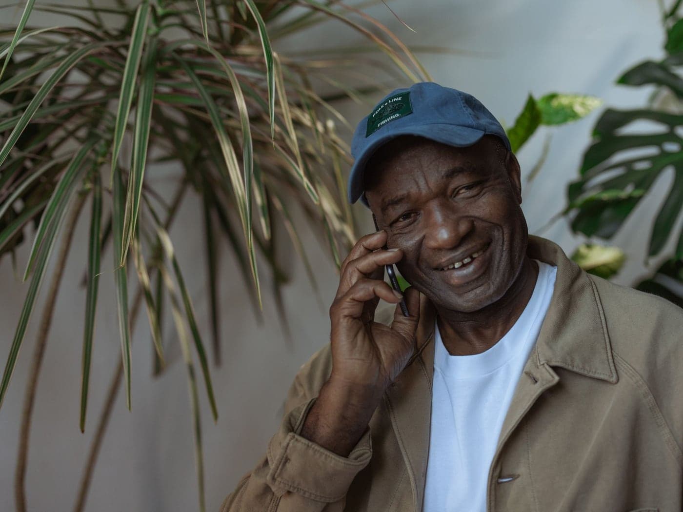 An older man in a cap smiling as he talks on his phone