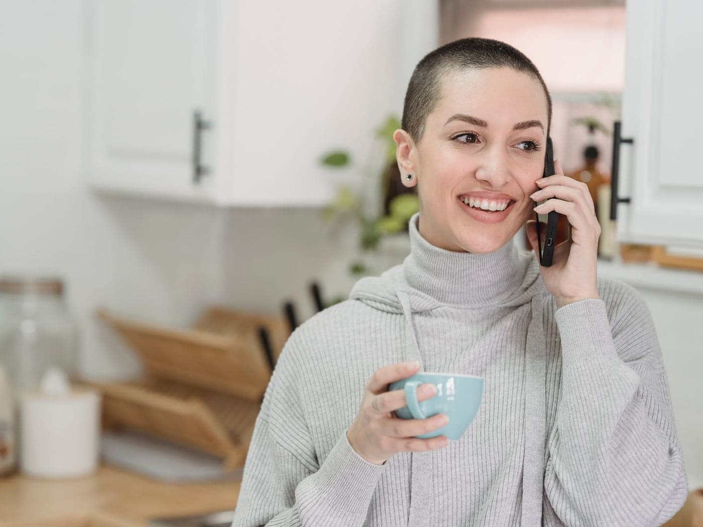 A smiling woman holding a mug while on the phone in her kitchen