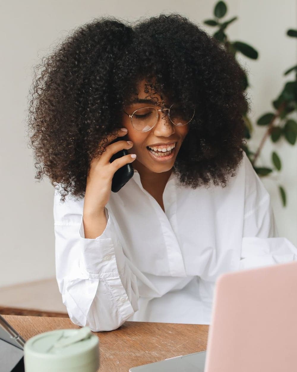 A smiling woman talking on her phone at a home desk with a laptop