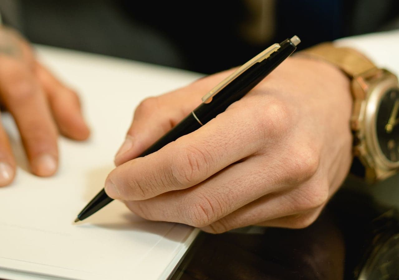 A hand signing a sheet of paper with a pen