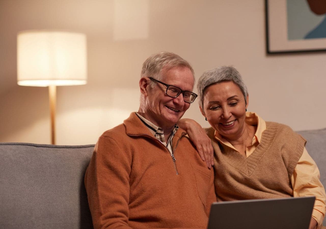 An older couple smiling as they look at a laptop together on a sofa